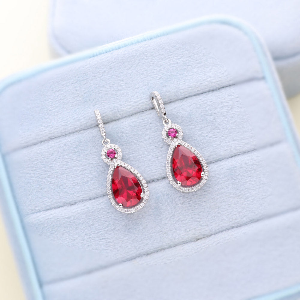 Flatlay view of Halo Simulated Ruby Pear CZ Dangle Earrings in Sterling Silver, 2 of 3