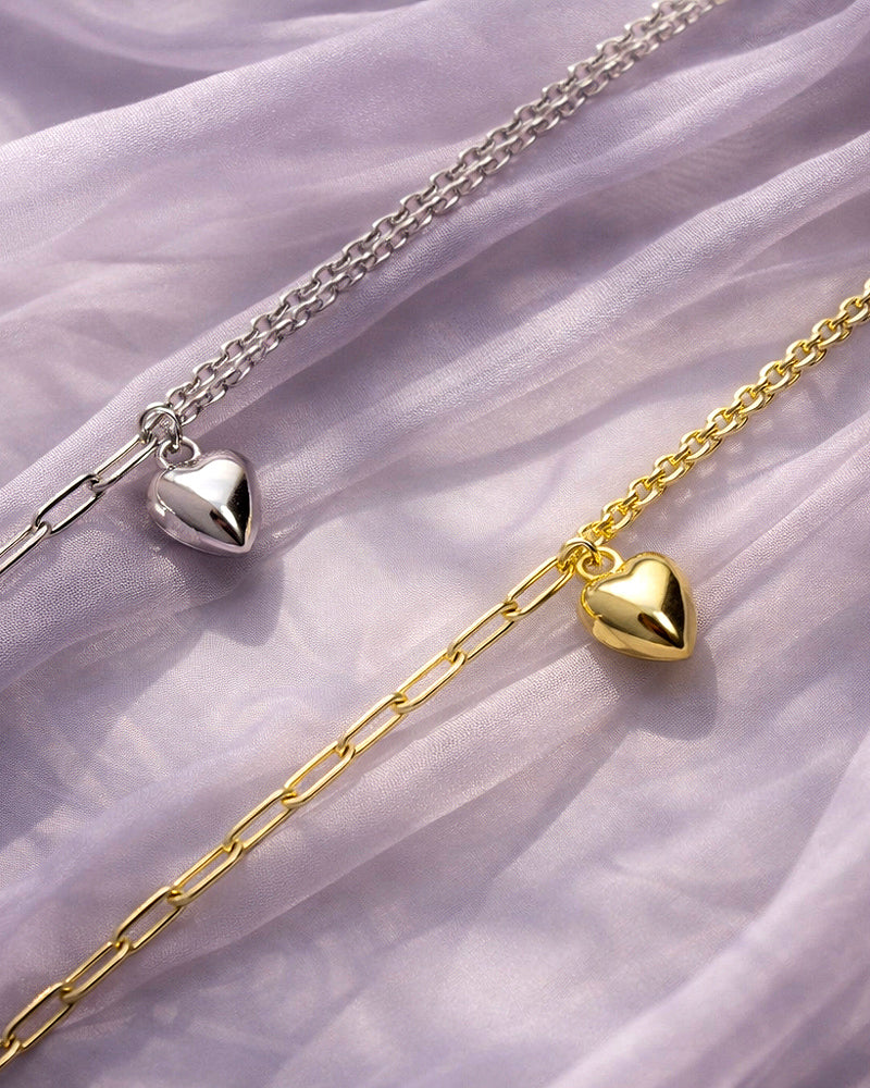 Gold and silver heart-shaped charm bracelets against a soft purple fabric background