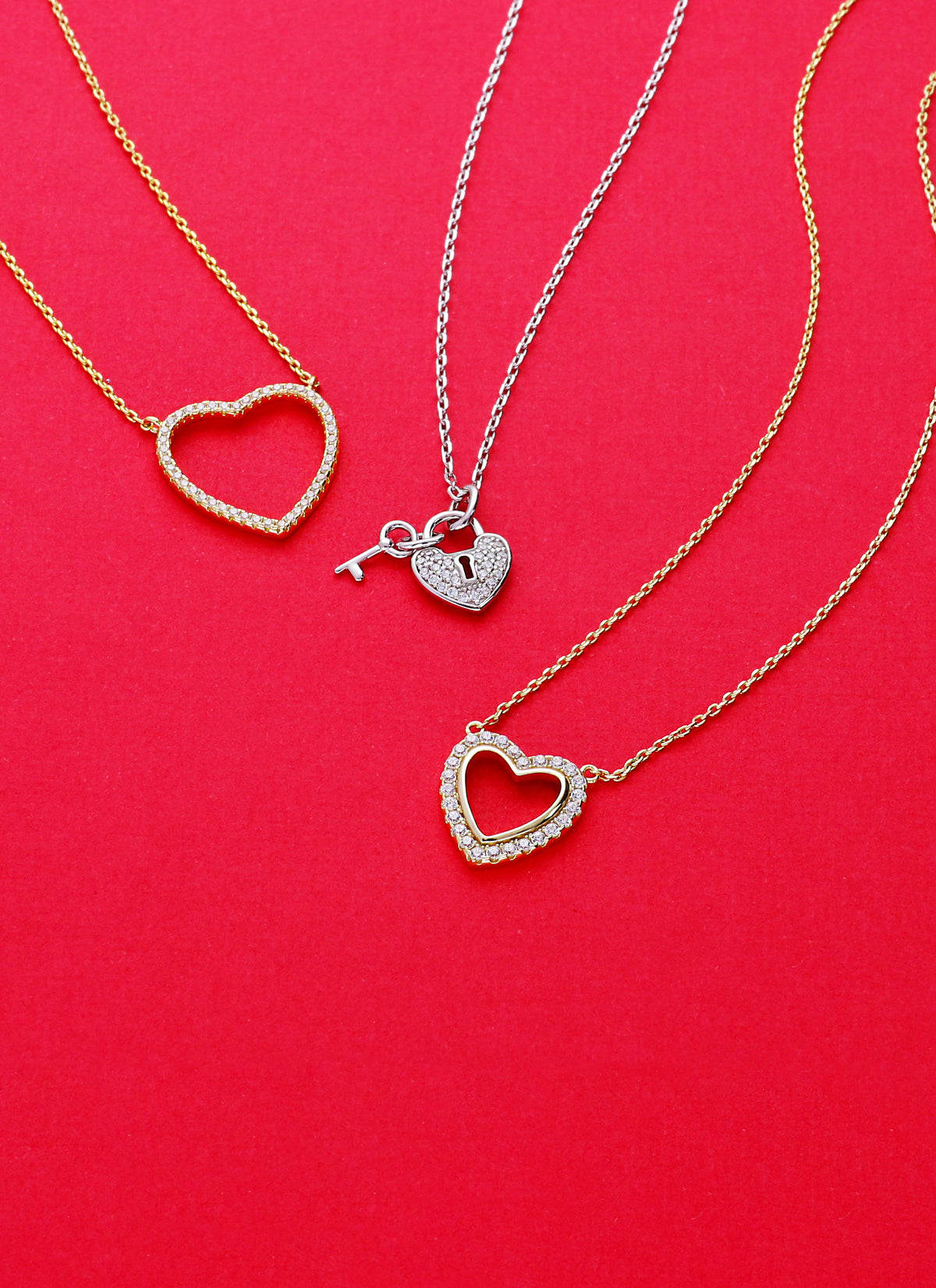 Three elegant heart-shaped necklaces displayed on a vibrant red background.