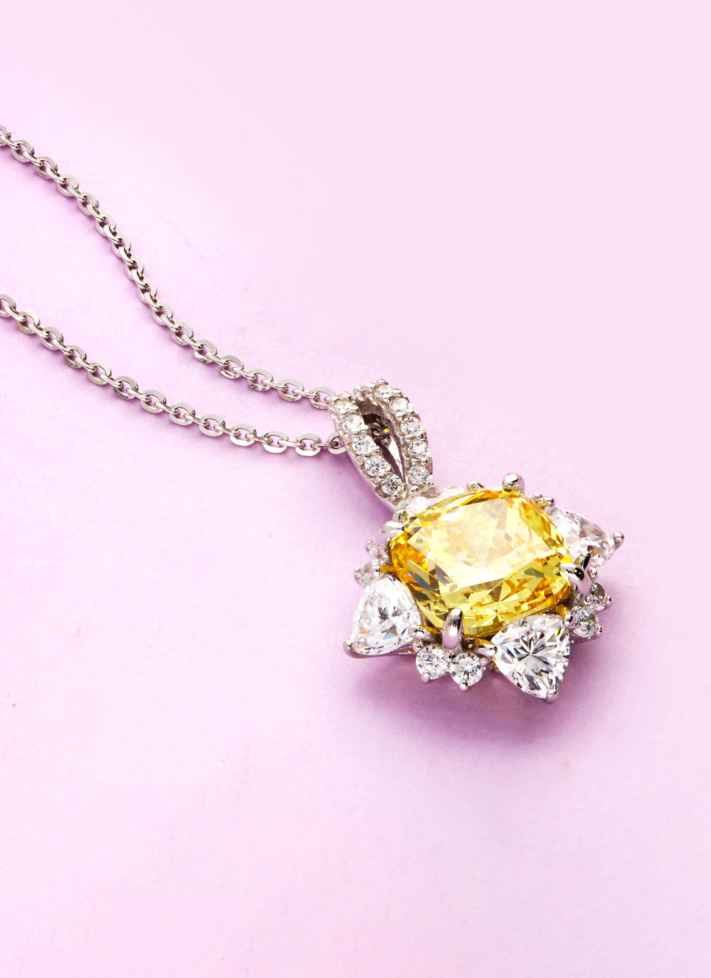 Elegant silver necklace featuring a radiant canary yellow CZ stone pendant, surrounded by sparkling white stones in a bold floral design, displayed against a soft pink background.