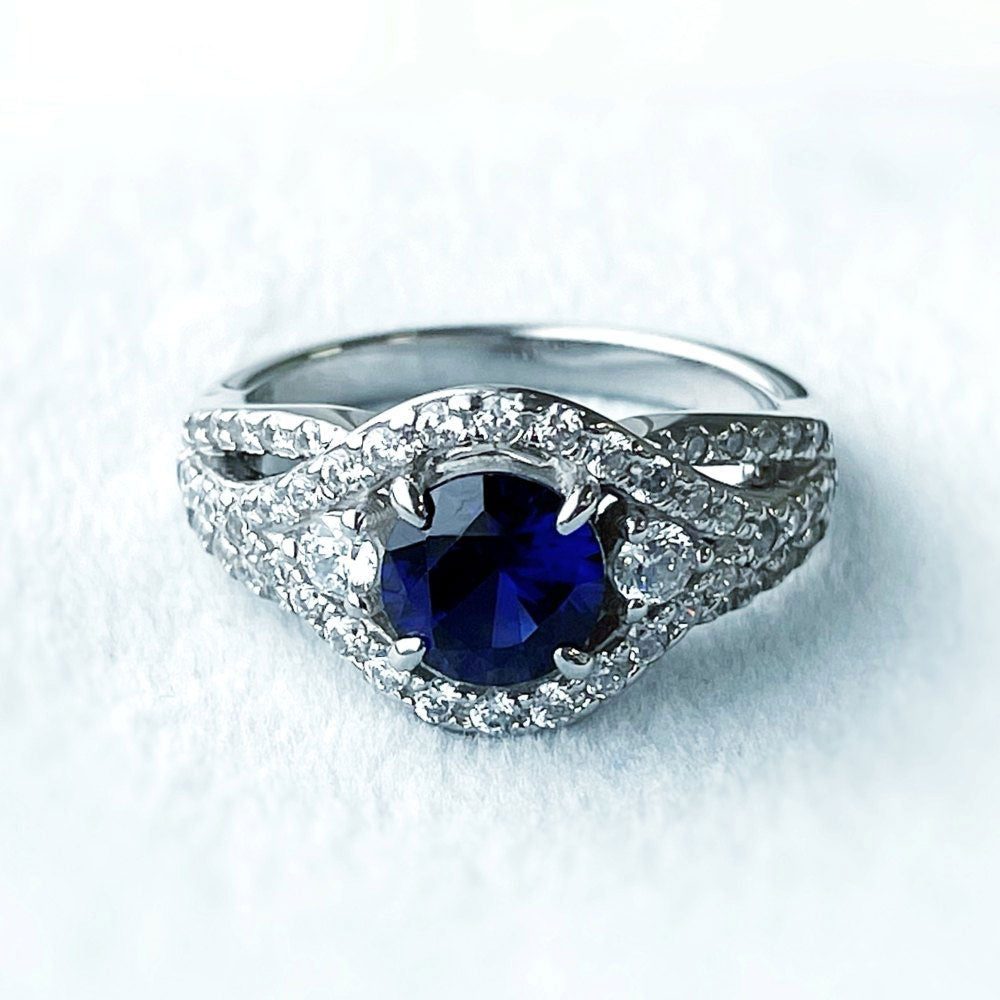 Flatlay view of 3-Stone Woven Halo Sapphire-Blue CZ Ring in Sterling Silver, 4 of 17